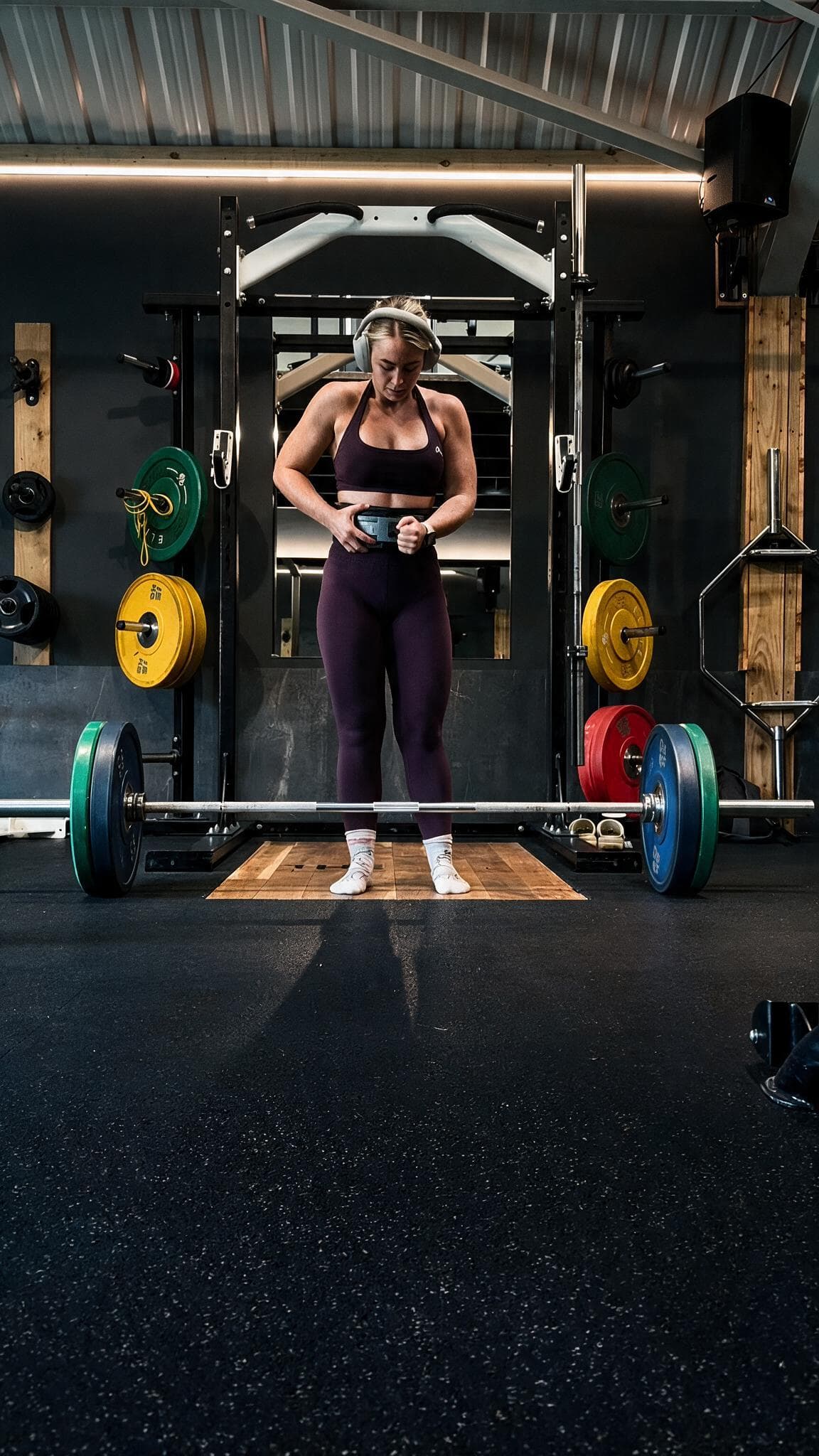 Beth fastening her lifting belt at a loaded barbell, set up to deadlift